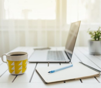 A laptop on a table with a cup of coffee